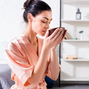 woman in bathrobe relaxing and sipping kava from a wooden coconut cup